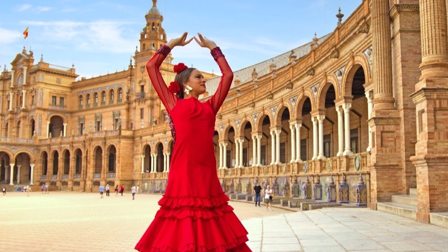 Flamenco dancer in red tiered dress posing before curved sandstone colonnade