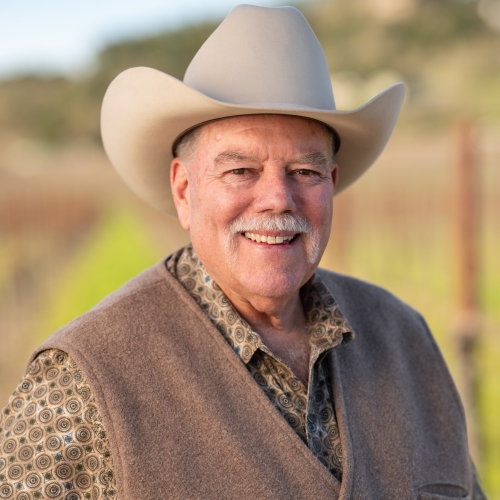 Smiling man in cowboy hat and vest, blurred rural background