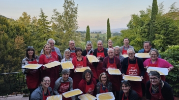 Smiling choir of ~20 in red scarves holding sheet music on a terrace at dusk