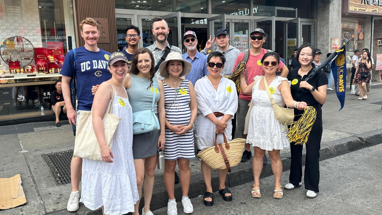 Fourteen smiling people in summer clothes on a city sidewalk outside New World Mall