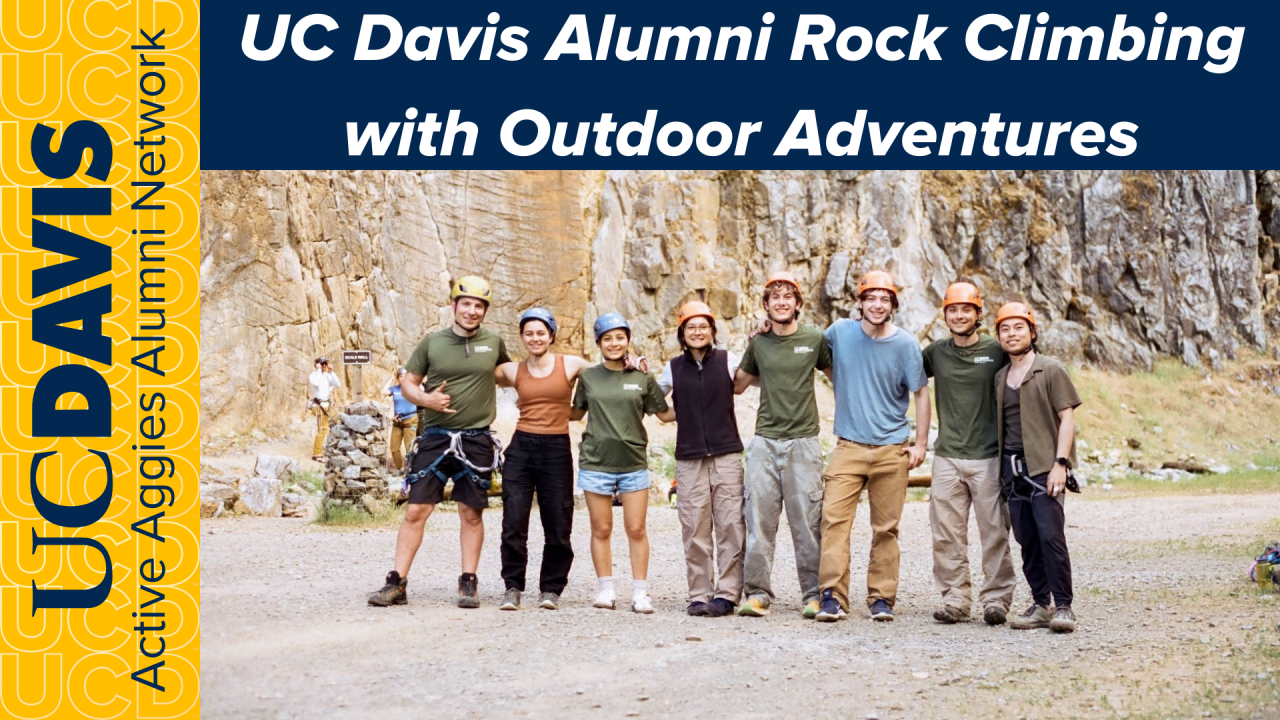 Group of people smiling together outdoors, wearing climbing gear, in front of rock formations.