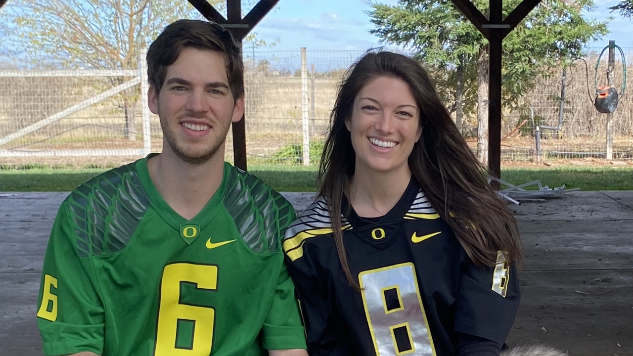 Smiling couple in football jerseys with white dog in red jersey under a pavilion