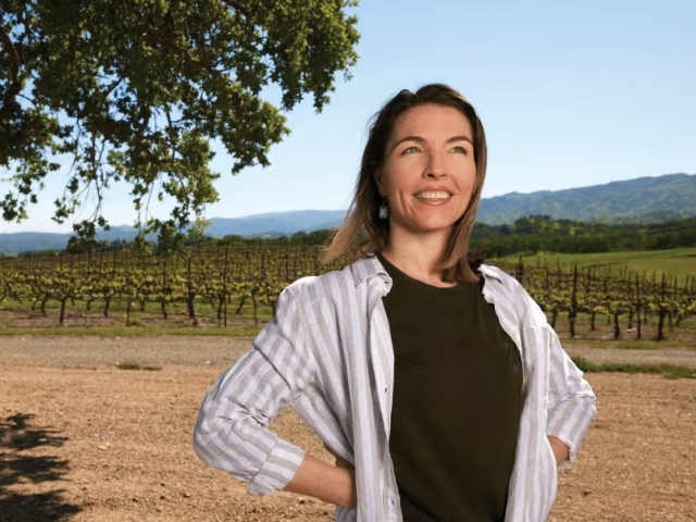 Smiling woman standing hands on hips in sunny vineyard with rolling hills