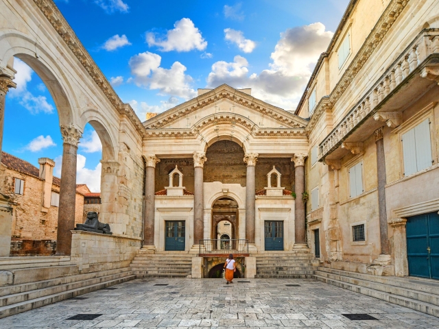 Historic courtyard with ornate architecture under a blue sky and scattered clouds.