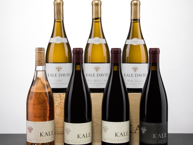Seven wine bottles on a tabletop: three white, three red, one rosé, white background.