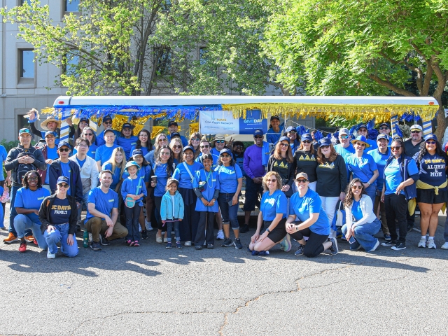 A large group of volunteers, staff and family dressed in matching UC Davis Give Day shirts pose in front of the decorated parade tram.