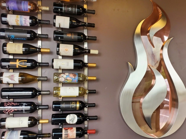Assorted wine bottles on wall rack beside a polished metal flame sculpture.