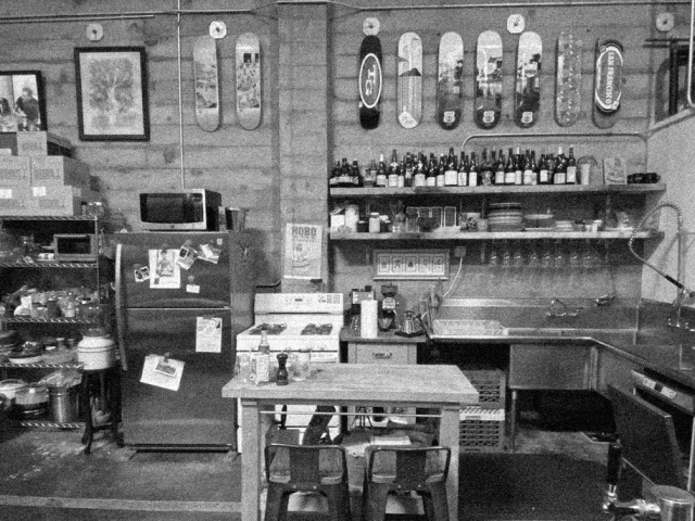 Black-and-white photo of a cluttered workshop with workbench, tools, and shelves