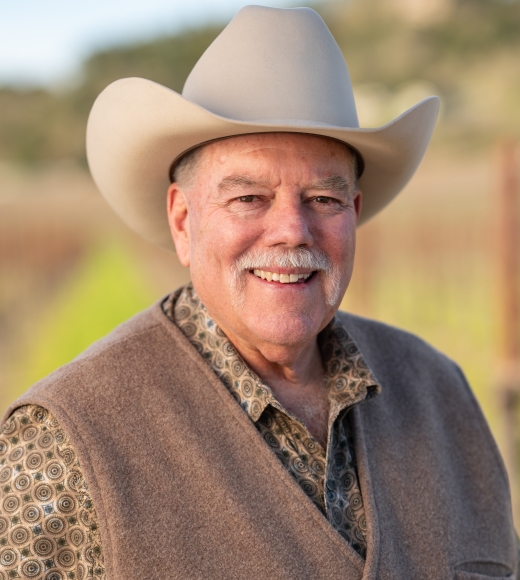 Smiling man in cowboy hat and vest, blurred rural background