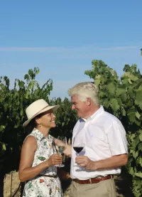 Jenny and Marcus Meadows-Smith look at each other while smiling and standing in the middle of vineyards.
