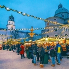 Festive market scene at dusk, crowded with people under twinkling lights.