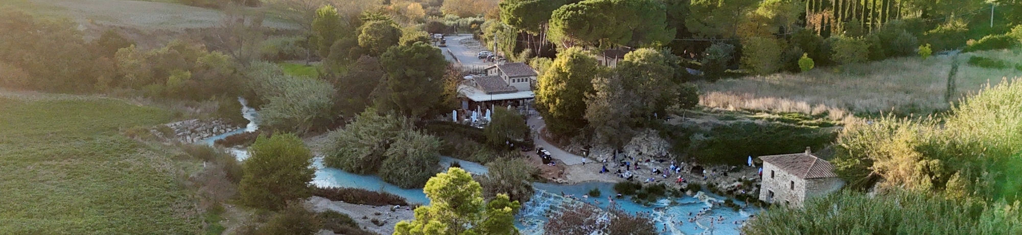 Aerial view of terraced blue pools and waterfalls amid green fields and rolling hills